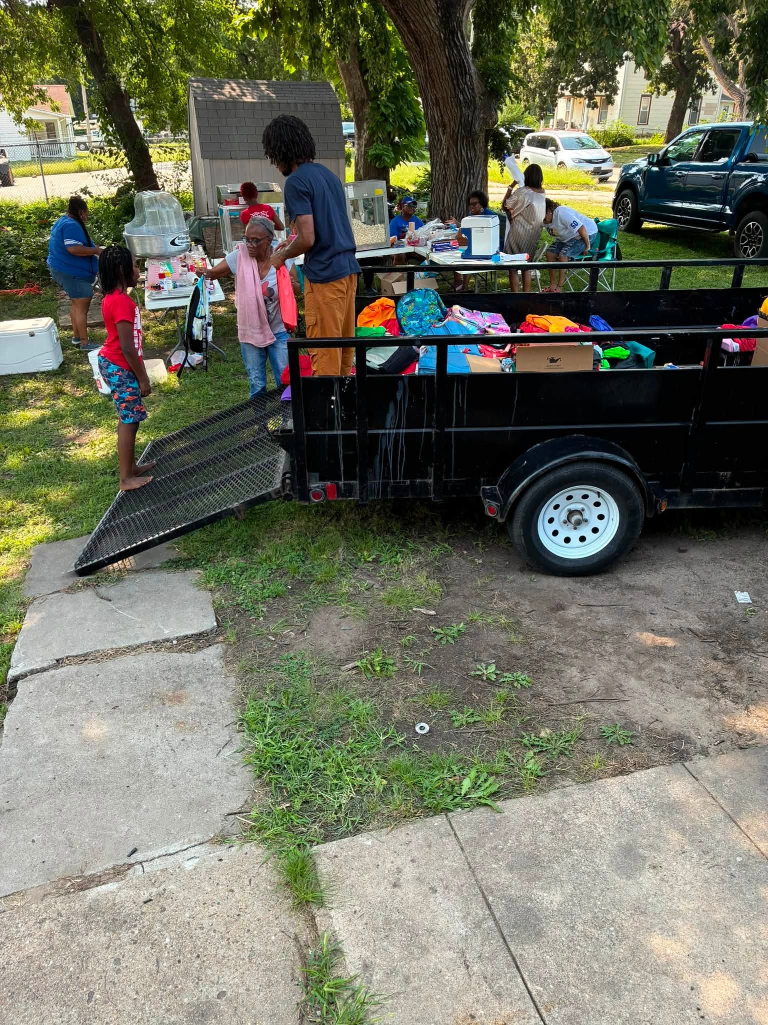 Volunteers organize a trailer filled with colorful bookbags while families enjoy refreshments at the Back-to-School Drive