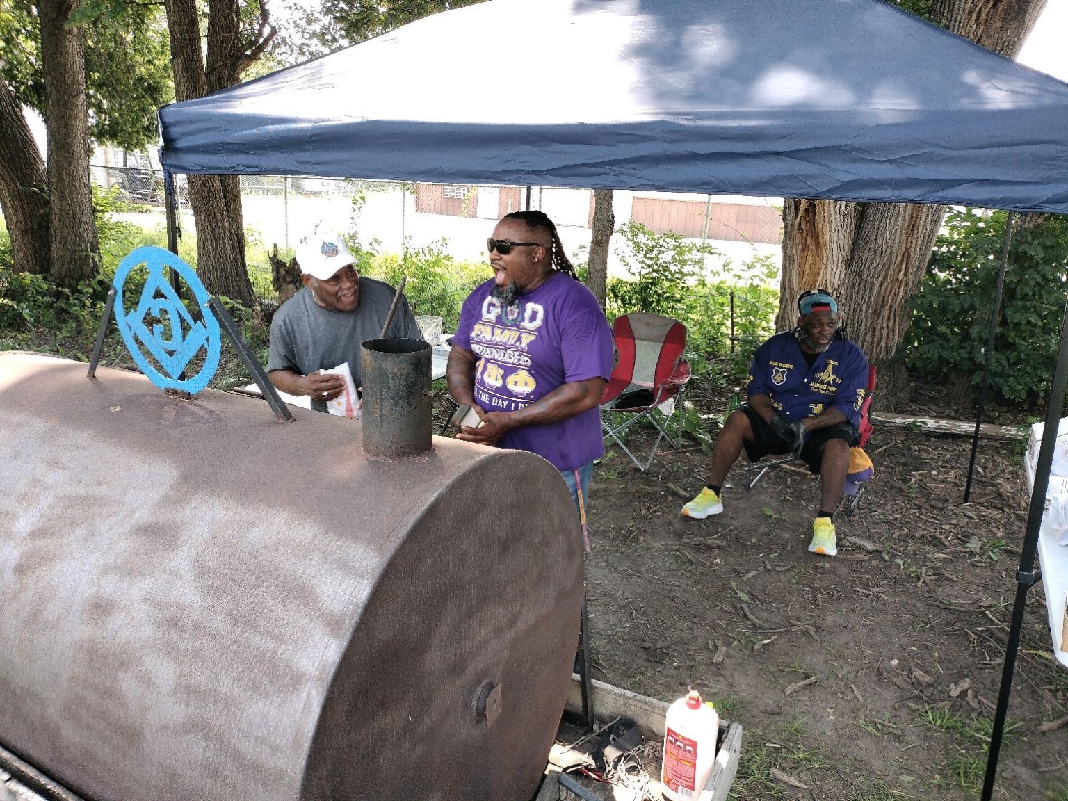 Brothers share a laugh while preparing food beside the lodge smoker